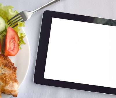 Tablet computer with blank isolated screen and dish with fresh salad on the restaurant table background. Electronic menu mock up. Food order online.